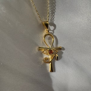 Op de afbeelding: Een gouden ketting met een ankh-hanger met een rood oog van Horus.