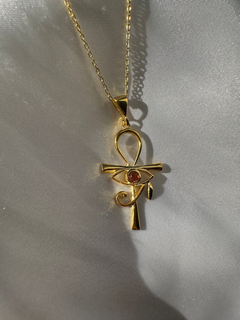 Op de afbeelding: Een gouden ketting met een ankh-hanger met een rood oog van Horus.