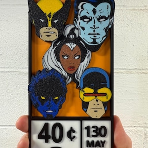 Puede incluir: Una obra de arte enmarcada con caras de personajes de cómics, incluyendo a Wolverine, Tormenta y Cíclope, sobre un fondo naranja. La parte inferior muestra el texto "40¢ 130 MAY 02061". El marco es negro.