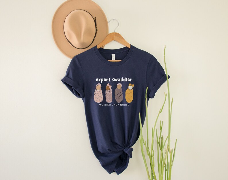 May include: Navy blue t-shirt with a white graphic of four swaddled babies and the text "expert swaddler" and "mother baby nurse".