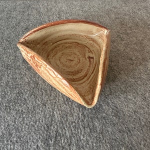 May include: A triangular ceramic dish with a brown and white speckled glaze. The dish has a slightly curved rim and a wide, shallow interior.
