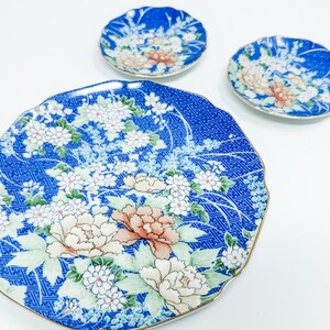 Puede incluir: Un juego de tres platos de porcelana azul y blanco con un diseño floral. Los platos tienen un borde festoneado y están decorados con flores blancas y hojas verdes sobre un fondo azul.