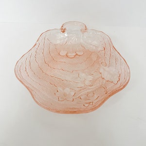 May include: A pink glass serving dish with a scalloped edge and a floral design. The dish has a handle on the top.