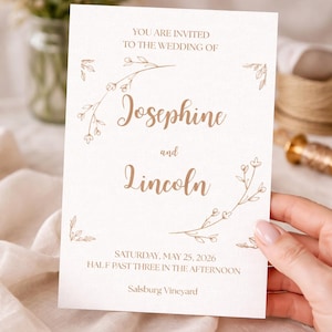 Könnte beinhalten: Eine weiße Keramik-Tasse mit schwarzem Henkel und dem Text "But First, Coffee" in fetter, schwarzer Schrift. Die Tasse steht vor einem verschwommenen Hintergrund, der eine gemütliche Umgebung suggeriert.