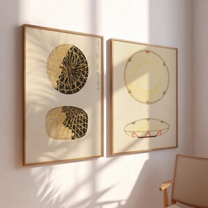 Puede incluir: Dos impresiones enmarcadas con diseños geométricos en negro y dorado. Las impresiones están en una pared blanca con una silla de madera en el fondo.