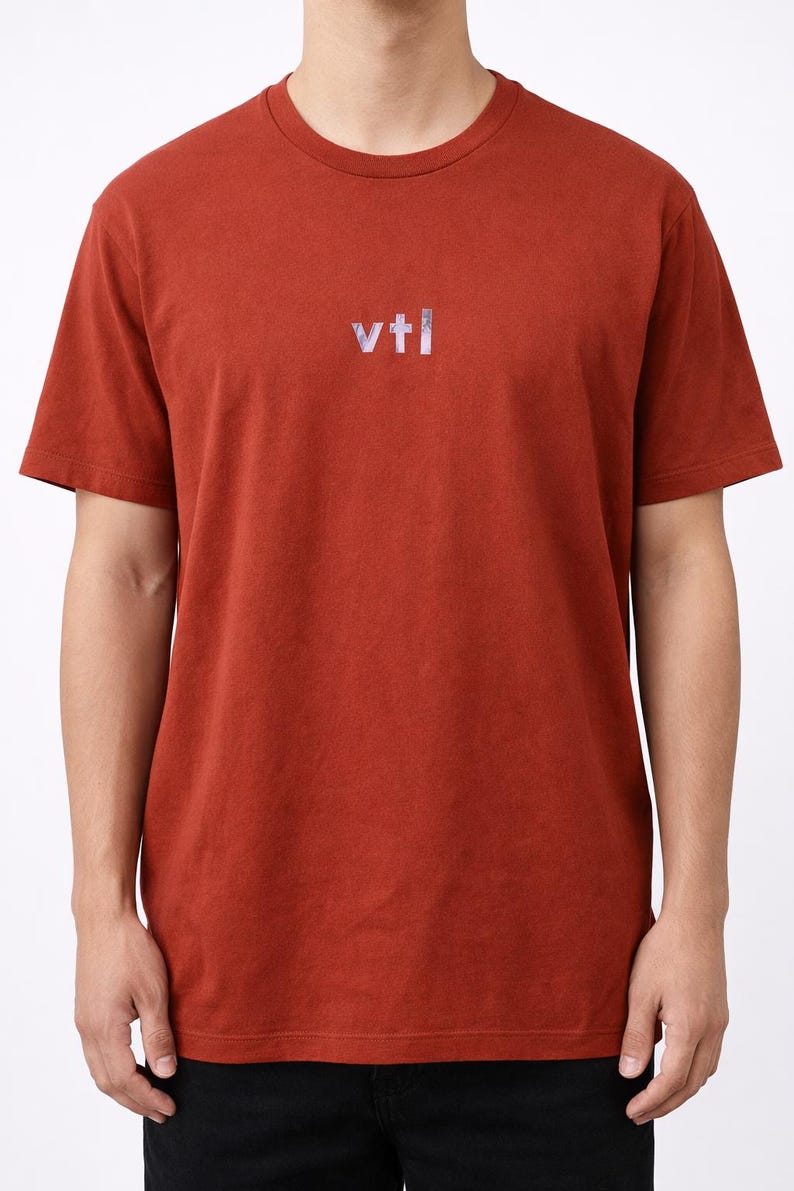 May include: Rust-colored short-sleeved t-shirt with the text "vtl" in a reflective, iridescent font across the chest. The shirt is made of a soft material and has a classic crew neck.