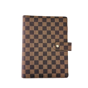 May include: A brown and black checkered pattern notebook with a snap closure. The notebook has a rectangular shape and a flap with a gold-colored snap. The pattern is a repeating grid of dark brown and black squares.