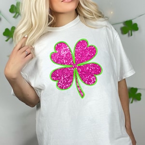Op de afbeelding: Wit T-shirt met een roze glitter vierklaverblad ontwerp omlijnd in groen.