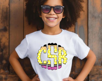May include: A white t-shirt with a yellow, black, and pink monogram design. The monogram is in the shape of a pencil and has the letters "CSR" in it.