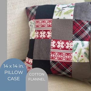 May include: A patchwork pillow case, 14 x 14 in., made of cotton flannel. The design features squares of various patterns, including red and black plaid, gray cable knit, and white fabric with red and green accents. The pillow is resting on a beige sofa.