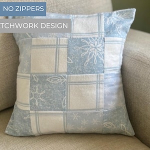 Può includere: Cuscino decorativo quadrato con un design patchwork in azzurro e bianco. Il cuscino presenta un motivo a griglia con disegni di fiocchi di neve e floreali. Il testo "NO ZIPPERS" e "PATCHWORK DESIGN" sono visibili.