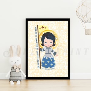 May include: A framed print featuring a cartoon illustration of Joan of Arc. She is depicted with dark hair, holding a banner with a cross and the text "I AM NOT AFRAID, I WAS BORN TO DO THIS." The background has a yellow floral pattern.