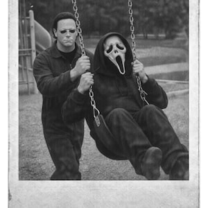 May include: Black and white image of two figures on a swing set. One figure wears a Scream mask and a black hoodie, swinging. The other figure, wearing sunglasses and a dark jumpsuit, pushes the swing. The image has a vintage, Polaroid-style border.
