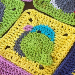 May include: Close-up of several colorful crocheted squares. The squares are in various colors, including yellow, green, purple, and blue. Each square features a different design, with some depicting a cartoon-like character. The crochet work is detailed and textured.