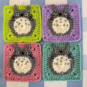 Pu&ograve; includere: Quattro quadrati all'uncinetto con un personaggio dei cartoni animati con occhi e orecchie grandi. I quadrati sono di colore verde, viola, rosa e turchese.