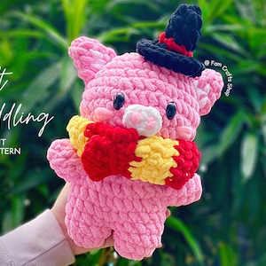 Może przedstawiać: Różowa dziana świnka w czarnym kapeluszu z czerwoną wstążką i czerwono-żółtym szalikiem. Świnka trzyma czerwono-żółty szalik w swoich przednich łapkach. Na zdjęciu widoczny jest tekst "Soft Cuddling" i "Instant PDF Pattern".