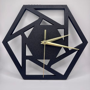 May include: Black geometric wall clock with gold-coloured hands. The clock has a hexagonal shape with a cut-out design.