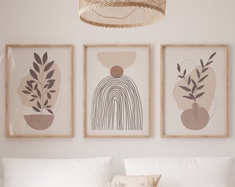 May include: Three minimalist abstract art prints in wooden frames, featuring brown and beige colors, with a white couch and a woven coffee table in the foreground.