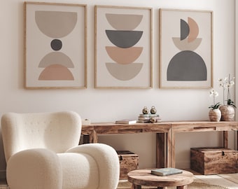 May include: Three framed abstract art prints with geometric shapes in neutral tones of beige, gray, and peach. The artwork hangs above a wooden console table with a white, rounded armchair and a round coffee table.