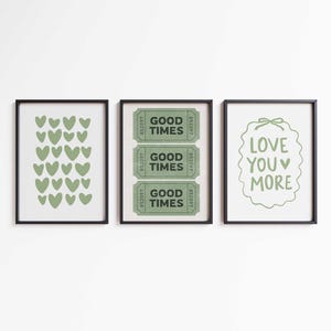 May include: Three framed art prints. The left print features green hearts. The center print displays three green "Good Times" tickets. The right print has the text "Love You More" in green. All prints are in black frames.