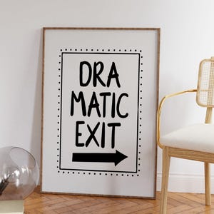 Op de afbeelding: Een rechthoekige ingelijste wandprint met een witte achtergrond en een zwarte rand van kleine stippen. De tekst "DRAMATIC EXIT" staat in een vet, handgeschreven zwart lettertype boven een effen zwarte horizontale pijl die naar rechts wijst.