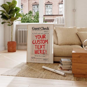 May include: A framed print of a guest check with the text "YOUR CUSTOM TEXT HERE!" in red. The print is displayed in a living room setting, leaning against a wall. The background includes a window, a sofa, and a plant.