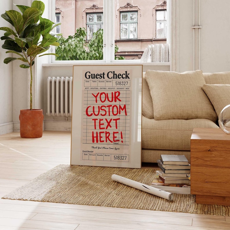 May include: A framed print of a guest check with the text "YOUR CUSTOM TEXT HERE!" in red. The print is displayed in a living room setting, leaning against a wall. The background includes a window, a sofa, and a plant.