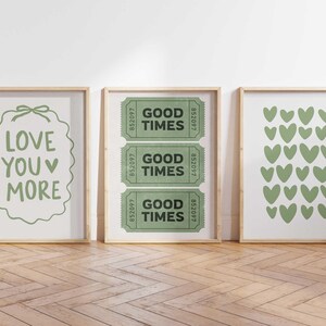 May include: Three framed art prints with light wood frames. The left print says "LOVE YOU MORE" in green. The middle print has three green "GOOD TIMES" tickets. The right print features green heart shapes.