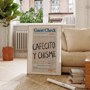 Pu&ograve; includere: Una stampa incorniciata di un conto del ristorante con le parole "CAFECITO Y CHISME" in grandi lettere scritte a mano. La stampa &egrave; in una cornice dorata e poggia su un tappeto intrecciato vicino a una finestra e a un divano.