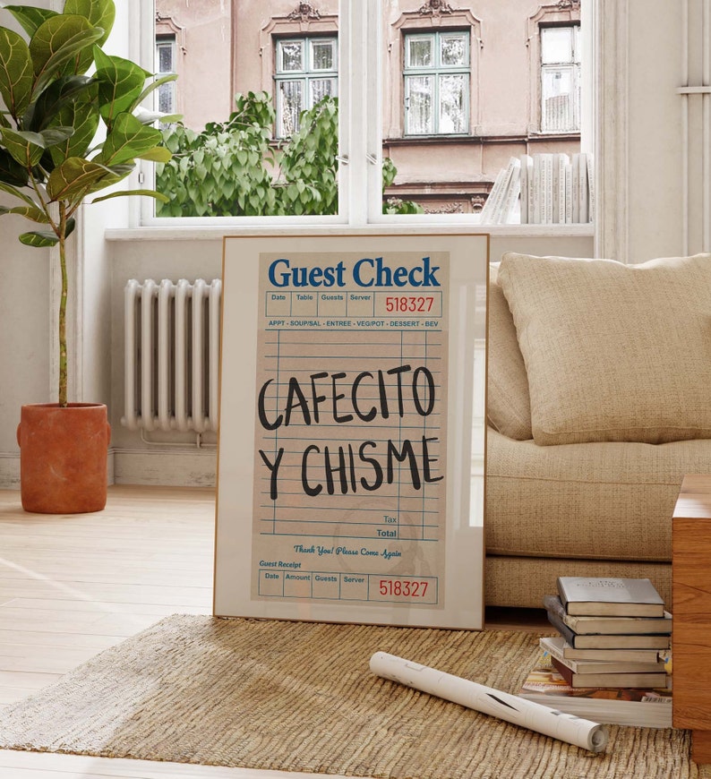 Pu&ograve; includere: Una stampa incorniciata di un conto del ristorante con le parole "CAFECITO Y CHISME" in grandi lettere scritte a mano. La stampa &egrave; in una cornice dorata e poggia su un tappeto intrecciato vicino a una finestra e a un divano.
