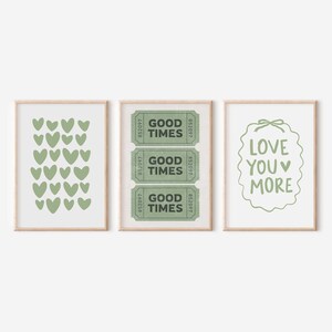 May include: Three framed art prints with a light wood finish. The prints feature a green heart pattern, three green "Good Times" tickets, and the phrase "Love You More" in green. The prints are on a white background.