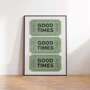 May include: A framed print featuring three green tickets with the words "GOOD TIMES" in bold black letters. Each ticket has the number "852097" printed on either side. The print is displayed on a white wall above a wooden floor.