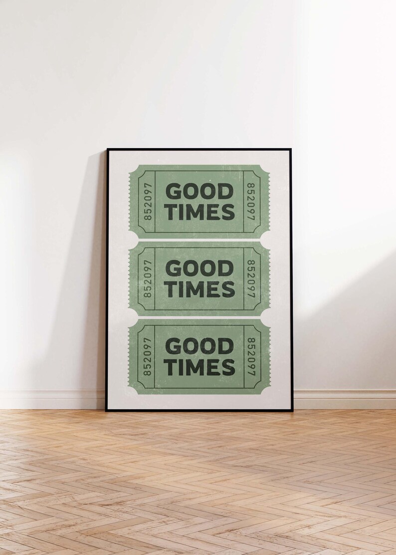 May include: A framed print featuring three green tickets with the words "GOOD TIMES" in bold black letters. Each ticket has the number "852097" printed on either side. The print is displayed on a white wall above a wooden floor.