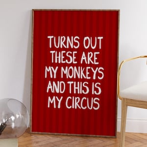 May include: A framed art print with a red background and white text that reads, "TURNS OUT THESE ARE MY MONKEYS AND THIS IS MY CIRCUS." The frame is a warm brown color. The print is displayed indoors.