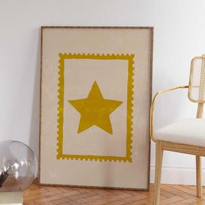 May include: A framed art print featuring a large yellow star within a yellow rectangular border, resembling a postage stamp. The star is centered on a beige background. The frame is a dark wood color.