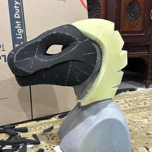 May include: A black and white foam head with a yellow foam crest. The head is marked with lines and numbers. The head is on a gray foam base.