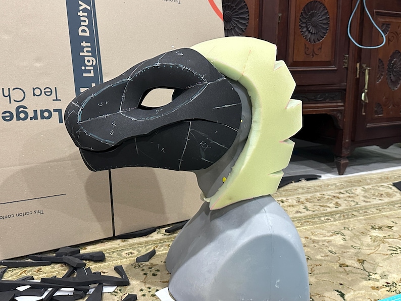 May include: A black and white foam head with a yellow foam crest. The head is marked with lines and numbers. The head is on a gray foam base.