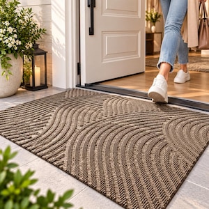 May include: A rectangular brown doormat featuring a textured surface with raised, repeating curved lines and geometric patterns. The mat is positioned on a light-colored tiled floor at the entrance of a doorway, displaying a durable, ridged design.