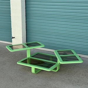 May include: A unique, lime green coffee table with three separate sections. Each section has a dark glass top and a rounded, geometric frame. The table is set on a concrete surface, with a teal-colored garage door in the background.