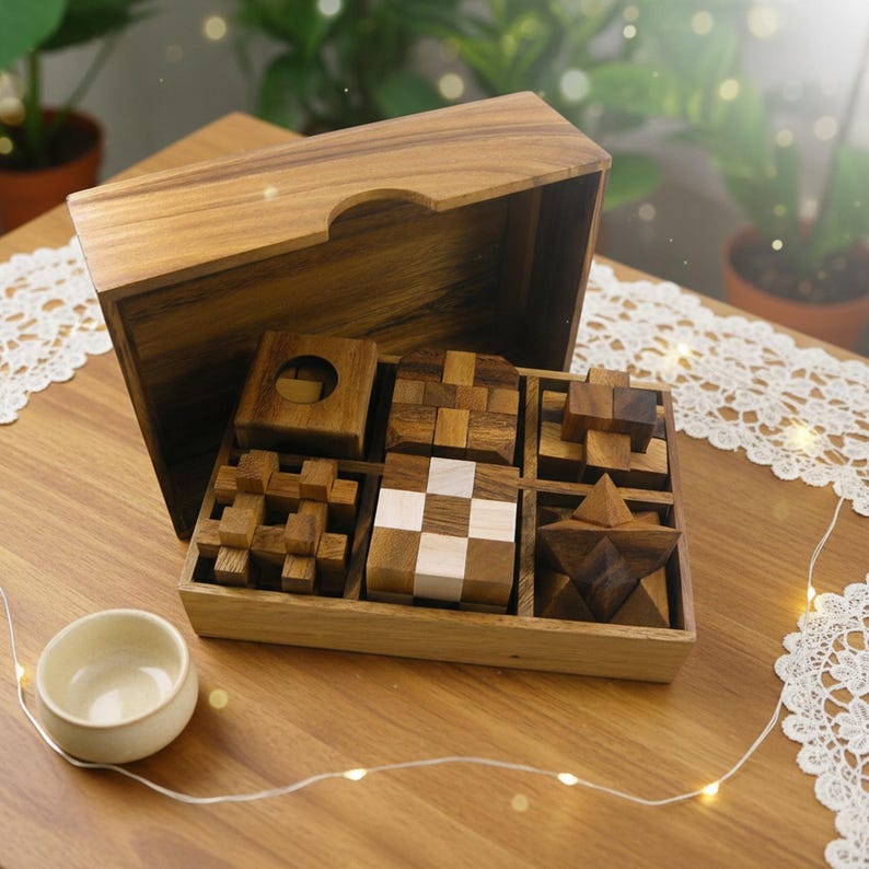 May include: A wooden puzzle set with various geometric shapes, including cubes, stars, and interlocking pieces, displayed in a wooden box. The set includes a small, off-white ceramic bowl. The wood has a warm, natural tone.