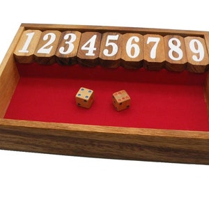 May include: Wooden game with numbered tiles and two dice. The tiles are arranged in a row, numbered 1 through 9. The dice are on a red felt surface inside the wooden box.