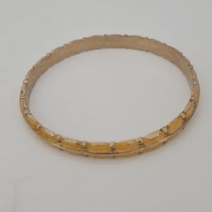 May include: A circular bangle bracelet featuring a two-tone design with alternating silver-colored metal segments and smooth, yellow-gold colored accents. The outer edge of the band has a repeating textured pattern with small raised metallic beads.