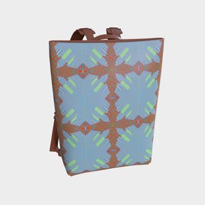 May include: A backpack featuring a geometric design in blue, orange, and green. It has brown straps and a handle. The pattern consists of intersecting lines and shapes, creating a repeating motif.