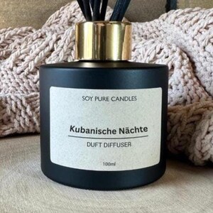 Könnte beinhalten: Ein schwarzer Sojawachs-Diffusor mit goldfarbenem Deckel und schwarzen Stäbchen. Das Etikett lautet "SOY PURE CANDLES" und "KUBANISCHE NÄCHTE DUFT DIFFUSER" mit einem Volumen von 100 ml. Der Diffusor steht auf einer Holzoberfläche.