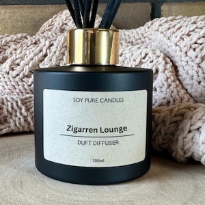 Könnte beinhalten: Eine schwarze Diffusorflasche mit goldfarbenem Deckel und schwarzen Stäbchen. Das Etikett lautet "Soy Pure Candles" und "Zigarren Lounge DUFT DIFFUSER 100ml."