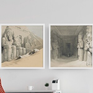 May include: Two black and white framed prints of ancient Egyptian statues. The first print shows a large statue of a seated pharaoh with a headdress. The second print shows a row of statues of pharaohs standing in a temple.