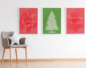May include: Three framed Christmas-themed art prints. One red print says "Love Peace Joy" in white script. The second print is green with a white Christmas tree. The third red print says "Merry Christmas" in white script. A gray chair with a star pillow is in the foreground.
