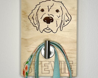 May include: A wooden dog leash hook with a laser-engraved image of a golden retriever's head. The hook has a silver metal hook and the name "Stevie" is engraved below the dog's head.