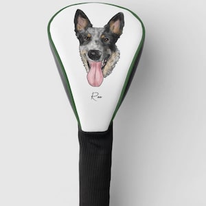 Könnte beinhalten: Weißer Golfschlägerkopfbezug mit grünem Besatz. Der Bezug zeigt eine Cartoon-Illustration eines Hundes mit blau-schwarzem Fell und einer herausgestreckten rosa Zunge. Der Name des Hundes, "Roo", ist darunter in Kursivschrift geschrieben.