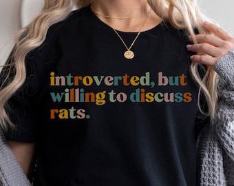 May include: Black t-shirt with the text "introverted, but willing to discuss rats." The text is in a retro font with colors including yellow, green, and orange. The shirt is a casual style.